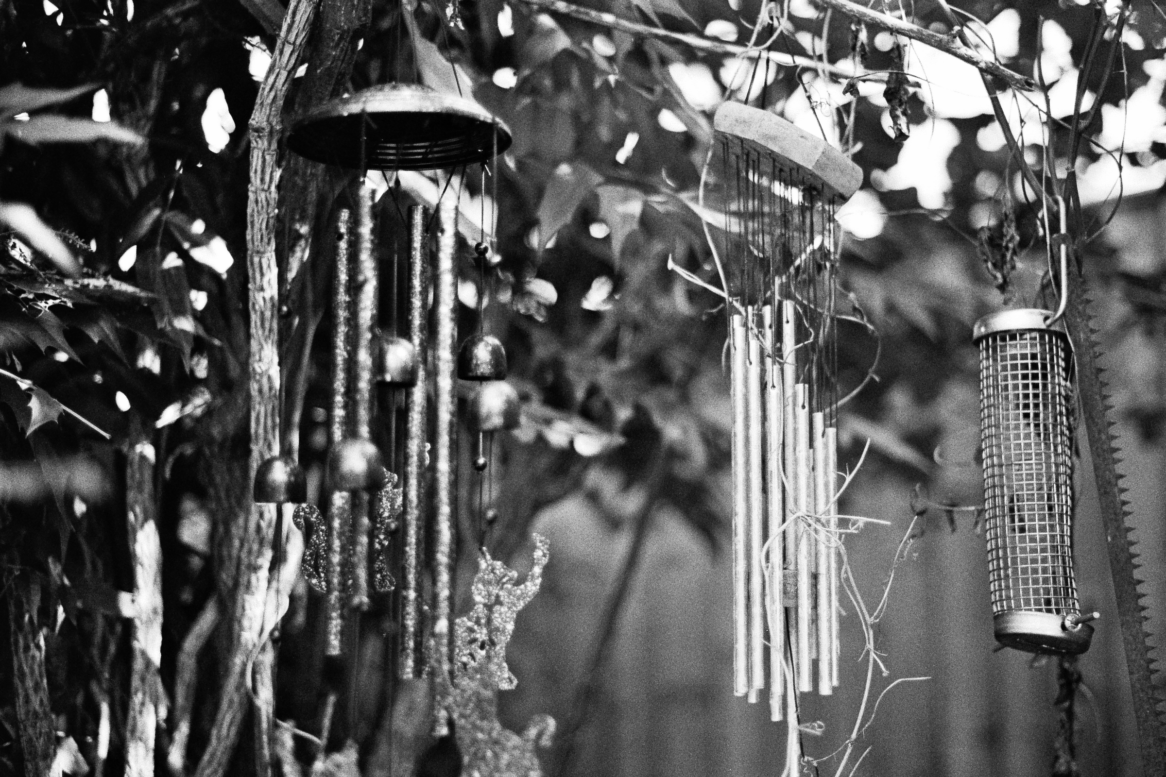 A black and white photograph of two wind chimes and a bird feeder