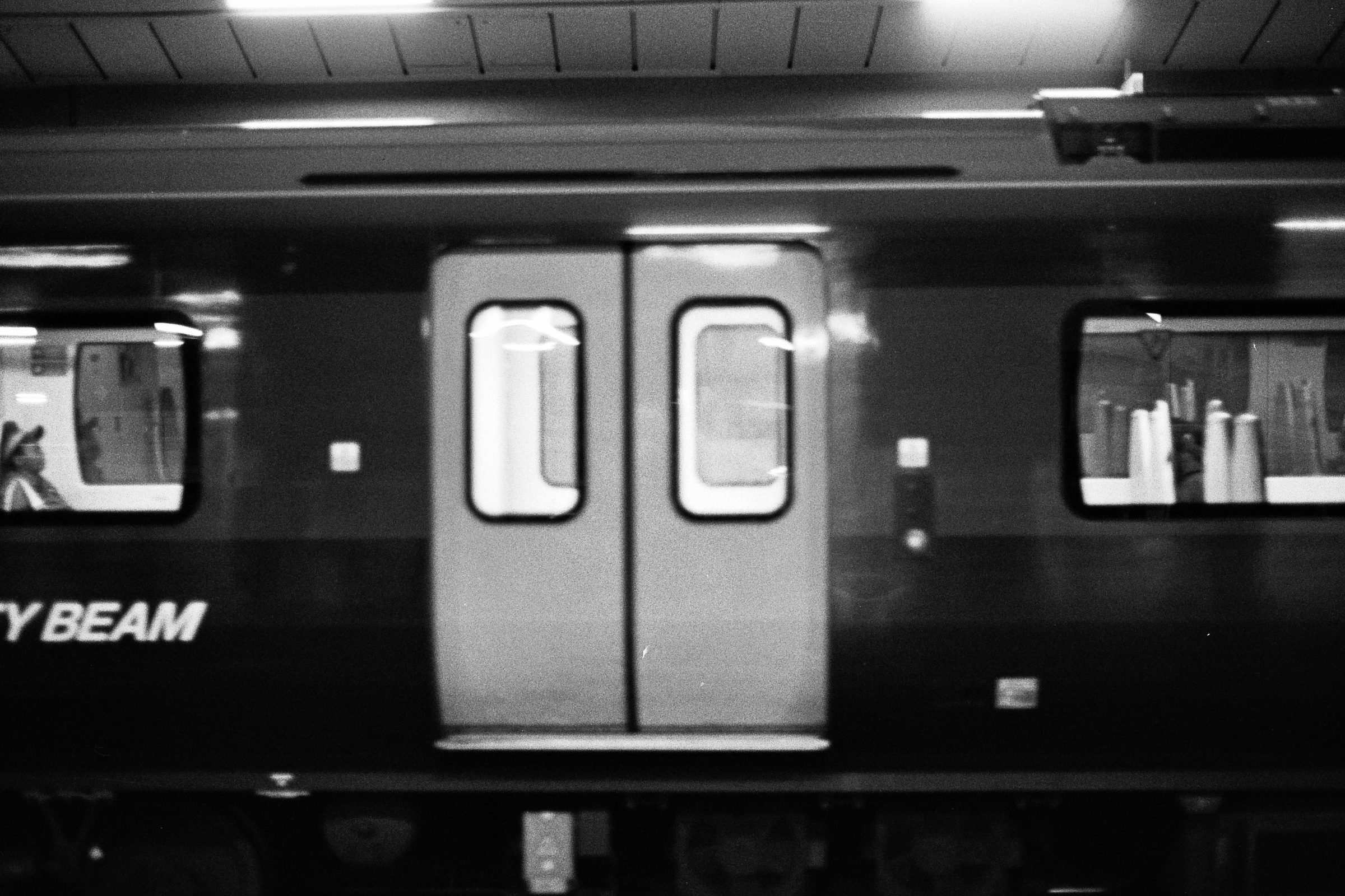 A black and white photograph of a train going through a station, with slight motion blur